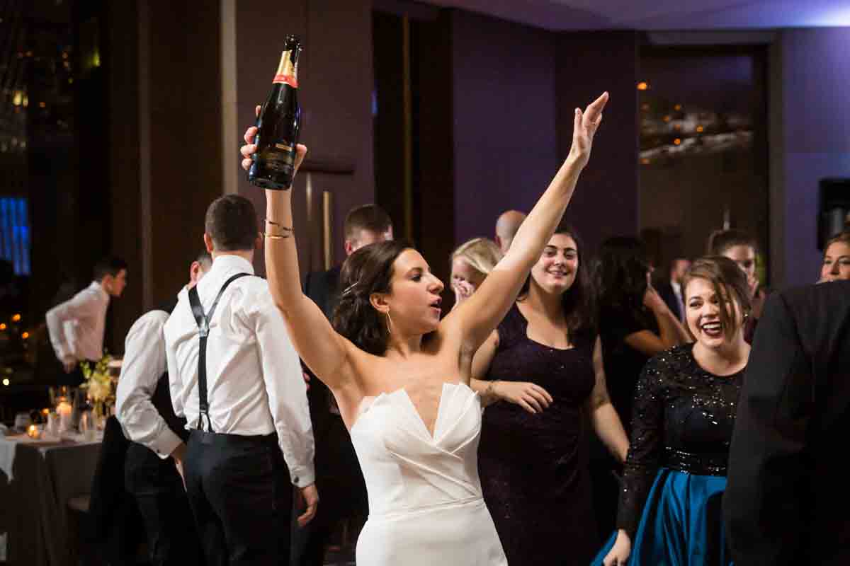 Bride holding up bottle of champagne at wedding reception