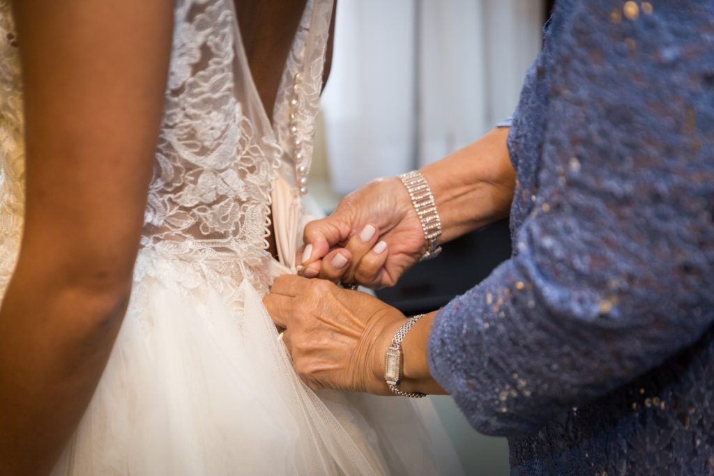 Close up on mother's hands zipping up bride's wedding dress