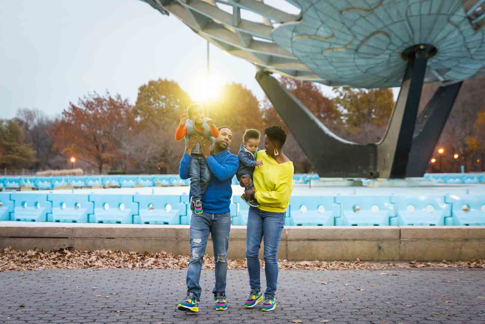 Flushing Meadows Corona Park family portrait of parents holding two children in front of Unisphere