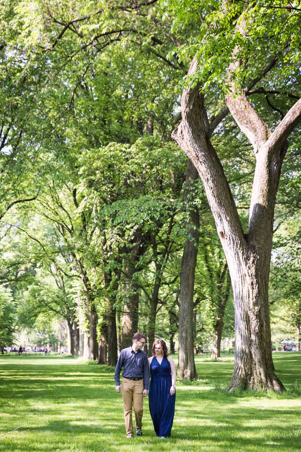Couple walking underneath trees at the Central Park Mall in Shakespeare Garden engagement photos