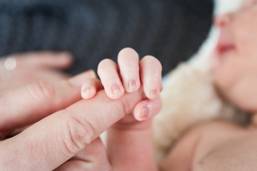 Close up of newborn baby hand holding adult finger