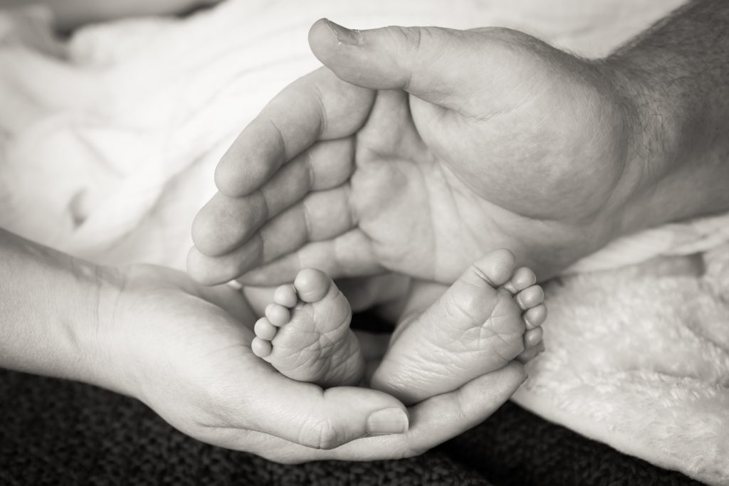 Black and white photo of newborn baby feet with hands of both parents