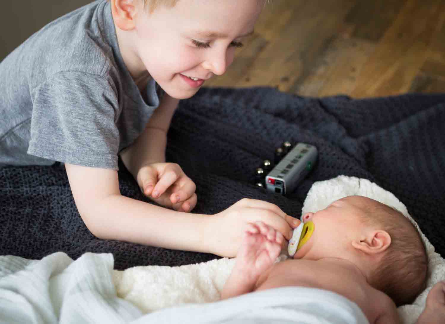 Little boy giving pacifier to newborn baby