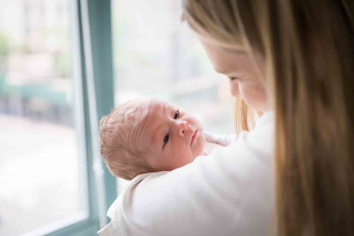 Mother holding newborn baby in front of window for an article on newborn portrait tips