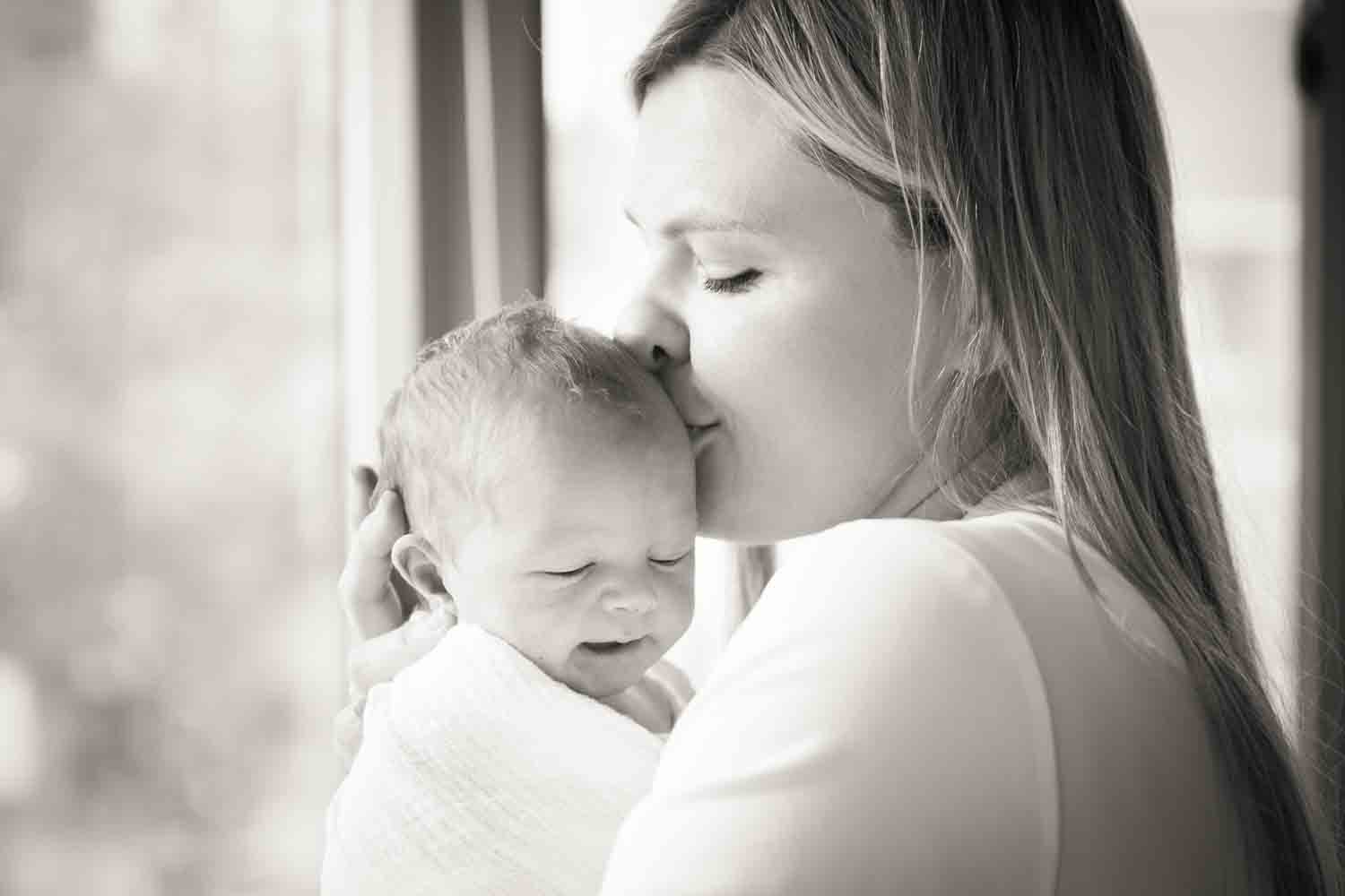 Black and white photo of mother kissing baby on side of head