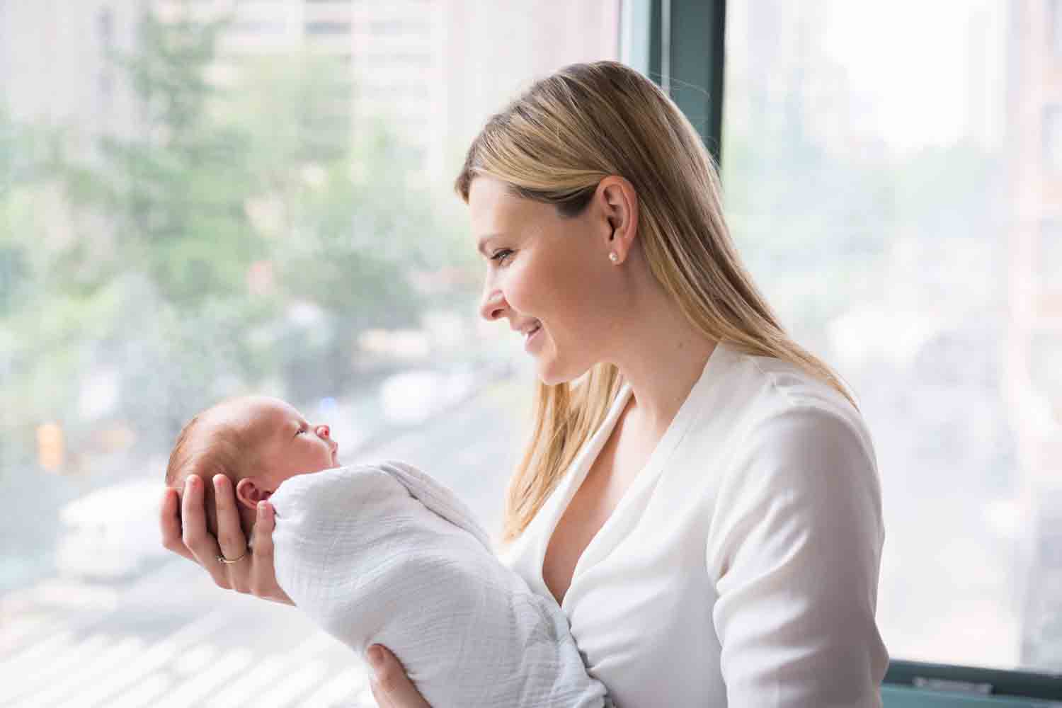 Mother holding newborn baby in front of window for an article on newborn portrait tips