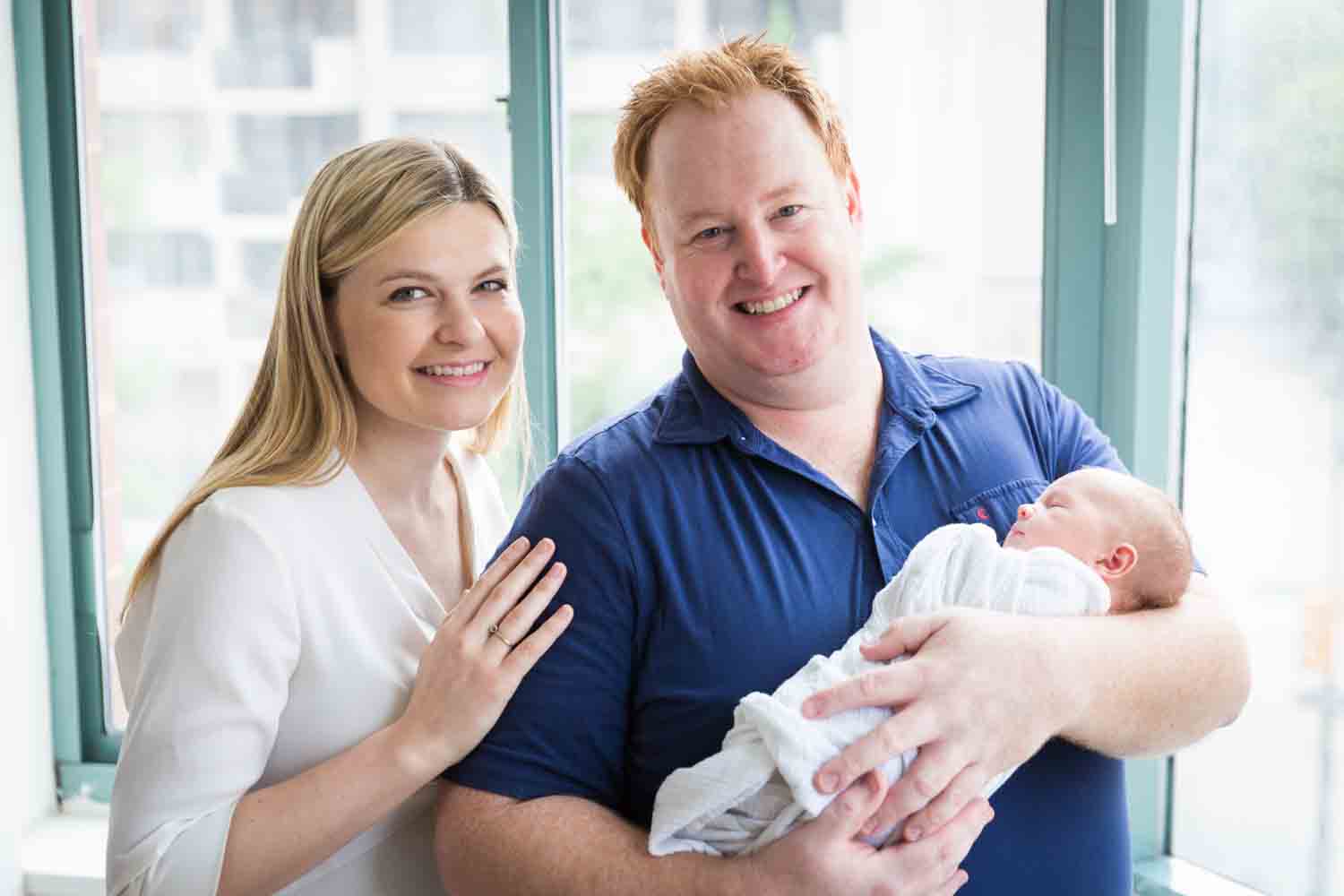 Parents holding newborn baby in front of window
