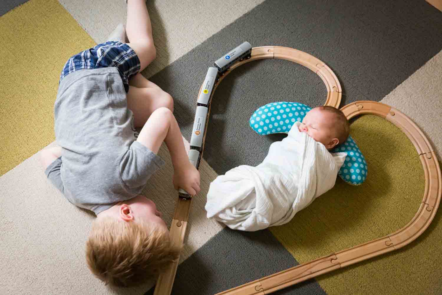 Little boy looking at newborn baby in middle of railroad toy set