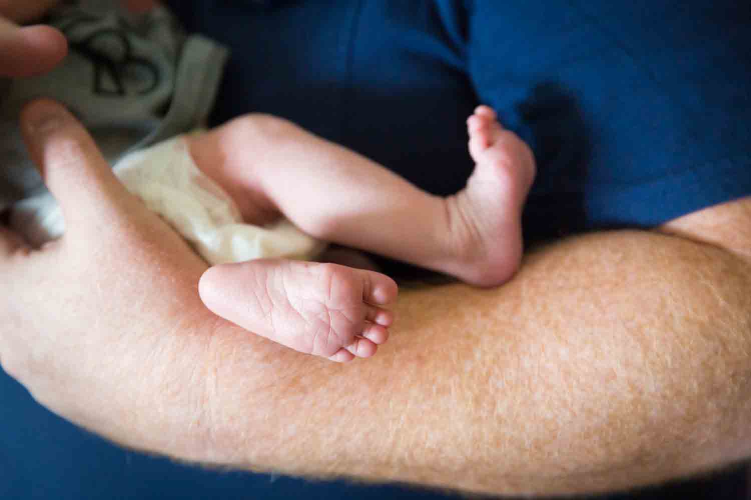 Close up of newborn baby feet against father's arm