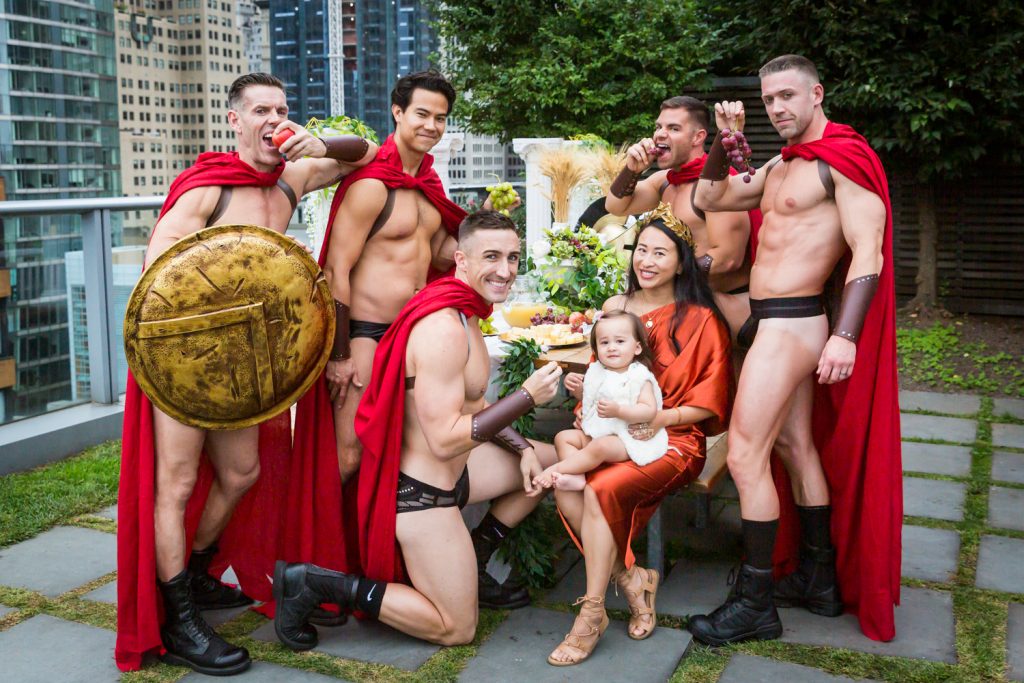 Birthday party photography of scantily clad men dressed as gladiators surrounding a little baby and mother