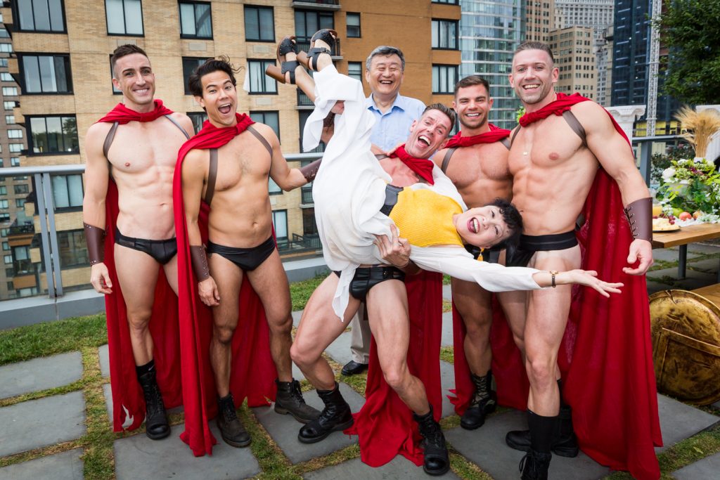Birthday party photography of men dressed as gladiators holding older woman upside down