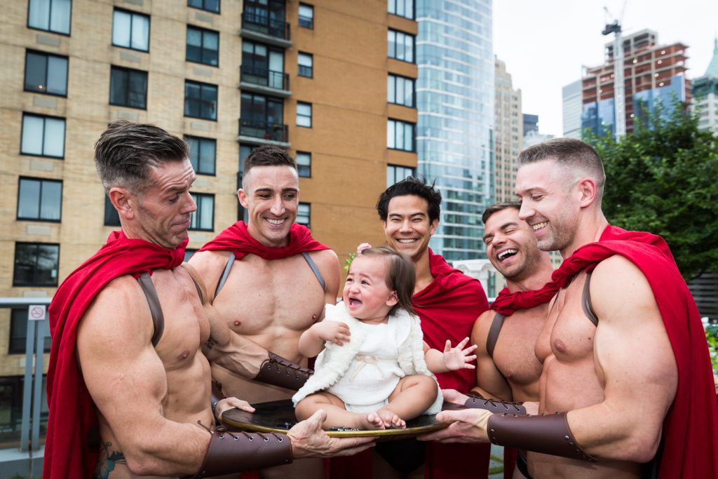 Birthday party photography of scantily clad men dressed as gladiators surrounding a crying baby