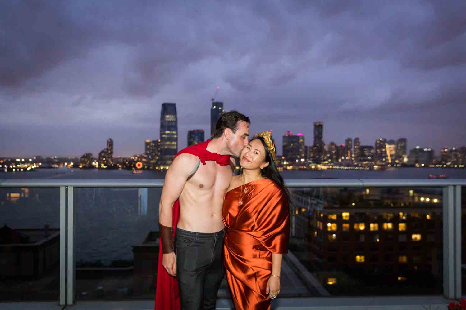 Man kissing woman at night wearing Roman outfit with NYC skyline in background