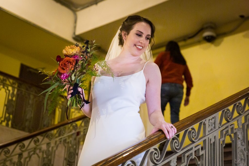 Bride holding flower bouquet on staircase looking down
