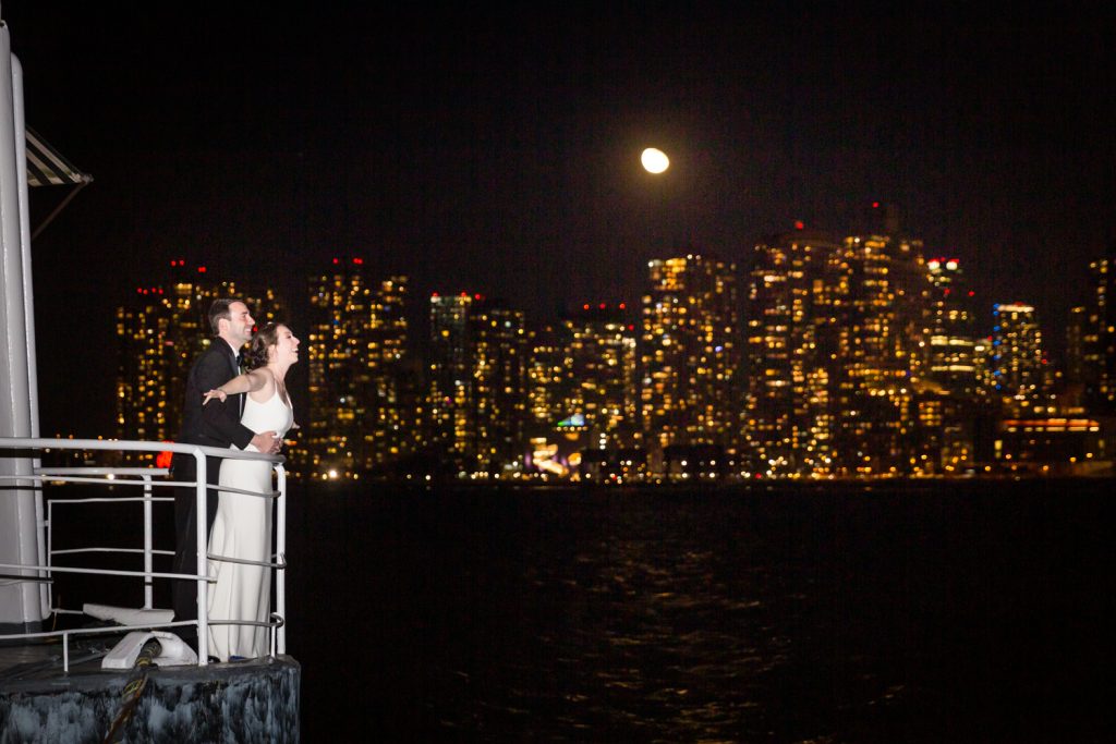 Bride and groom in Titanic pose with Queens skyline in background at a Water Club wedding