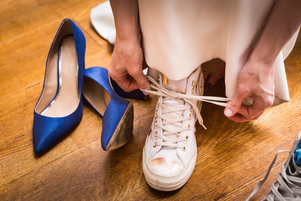 Close up of bride tying tennis shoe with blue heels to the left at a Water Club wedding