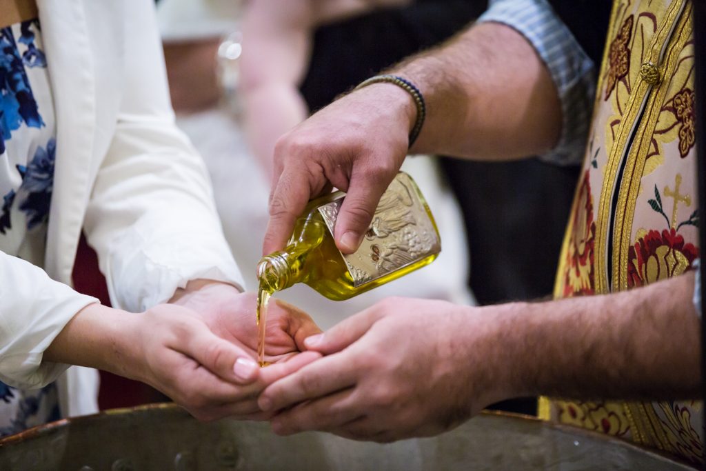 Close up of priest pouring oil into hands of godparent