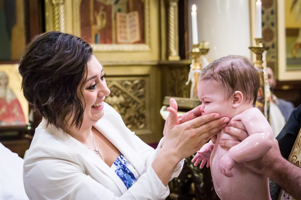 Greek orthodox baptism photos of godmother touching baby's cheeks