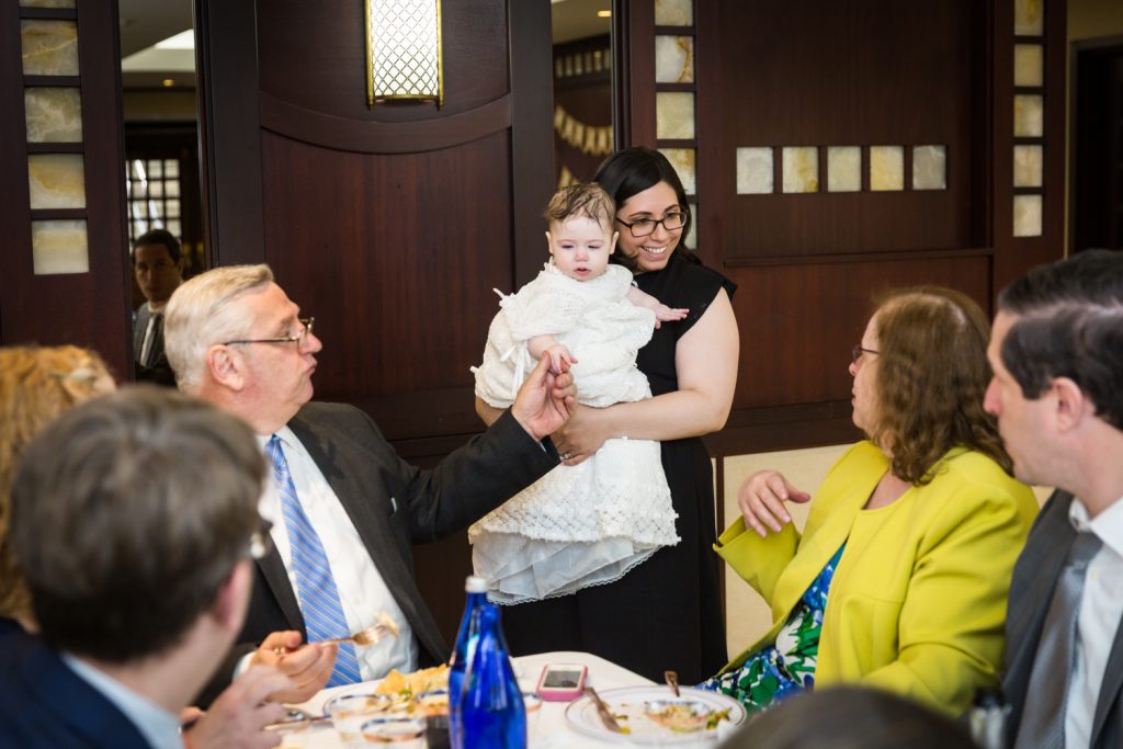 Mother showing off baby to table of guests at Greek orthodox baptism reception