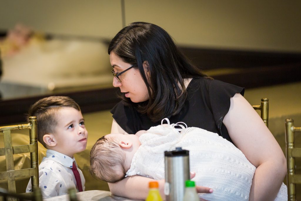 Mother holding baby and talking to little boy at Greek orthodox baptism reception