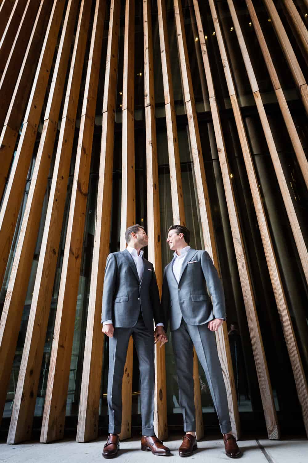 Greenpoint Loft wedding photos of two grooms standing in front of wall with wooden slats