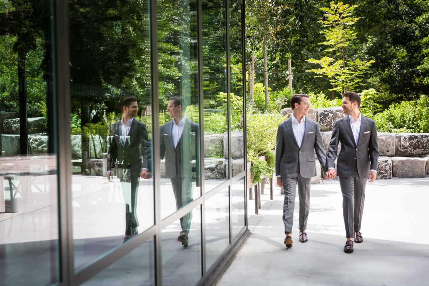 Greenpoint Loft wedding photos of two grooms walking hand-in-hand reflected in glass