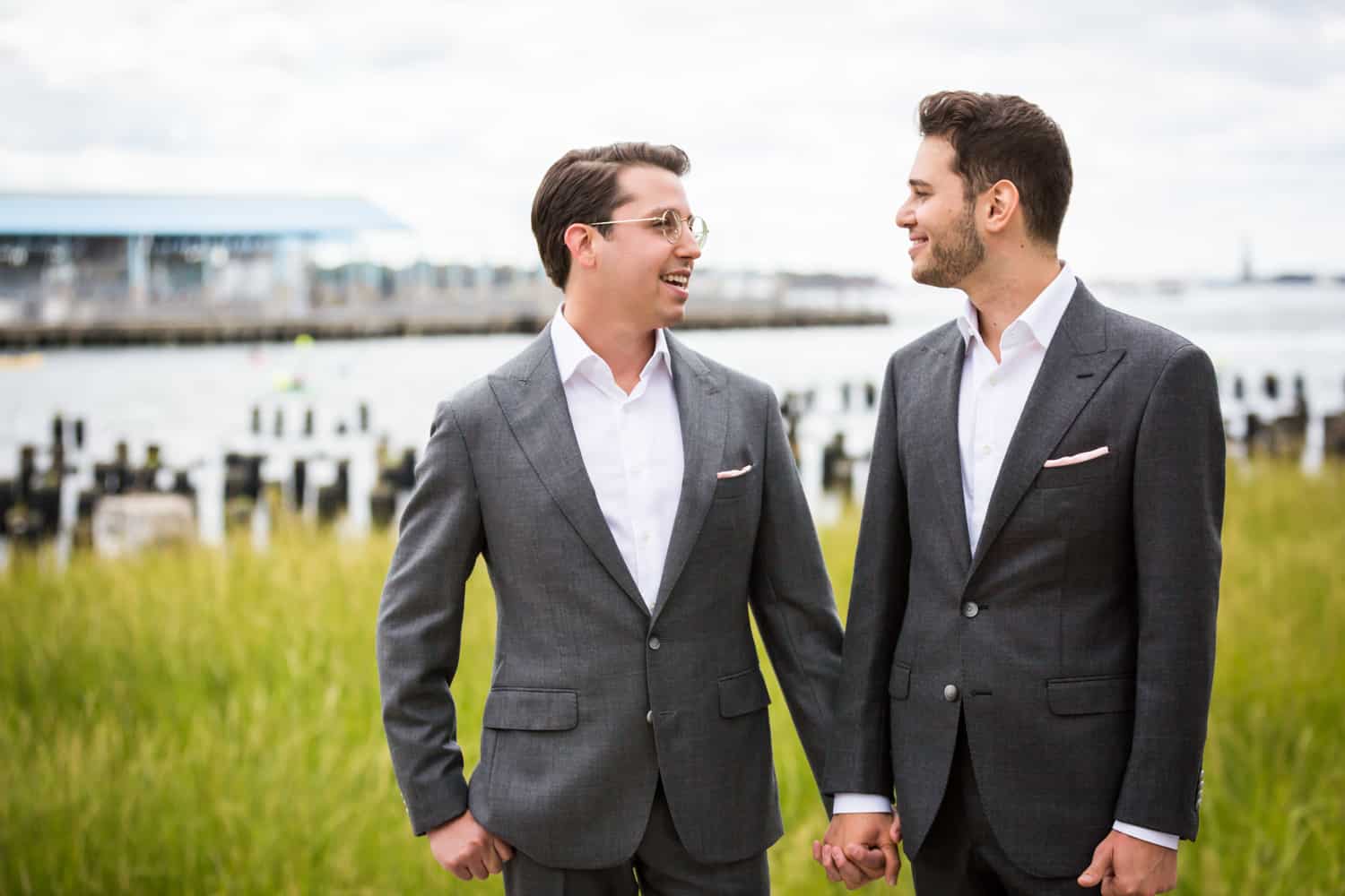 Greenpoint Loft wedding photos of two grooms holding hands in Brooklyn Bridge Park in front of Park Poles View