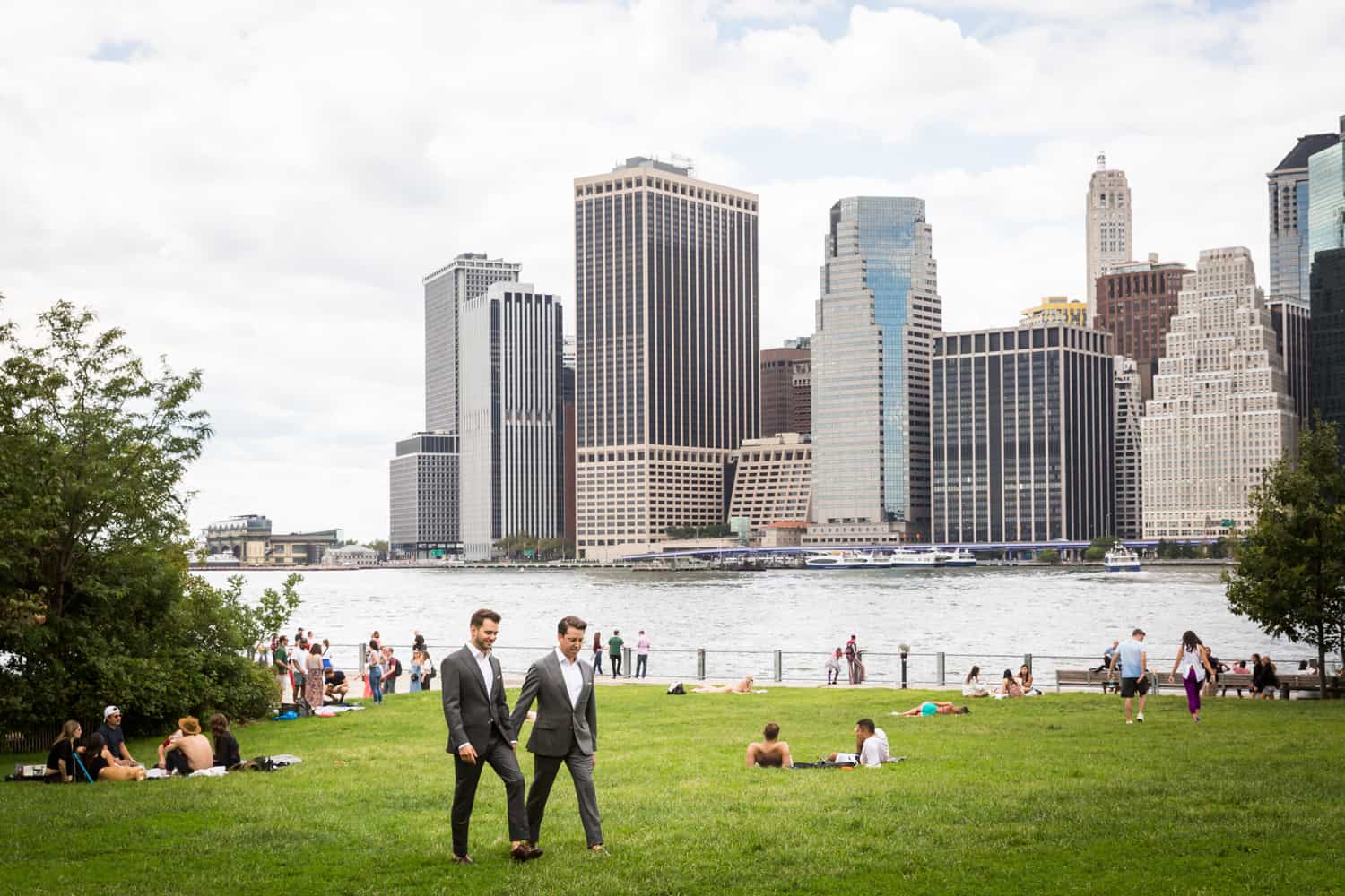 Greenpoint Loft wedding photos of two grooms walking across grass with NYC skyline in background