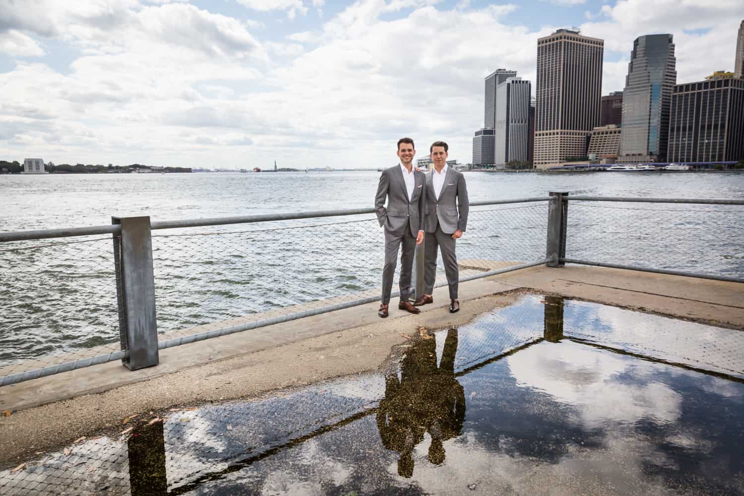 Greenpoint Loft wedding photos of two grooms at Brooklyn Bridge Park reflected in water puddle