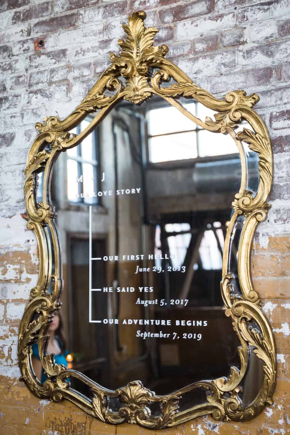 Gold-framed mirror on brick wall with love story timeline written on front of mirror