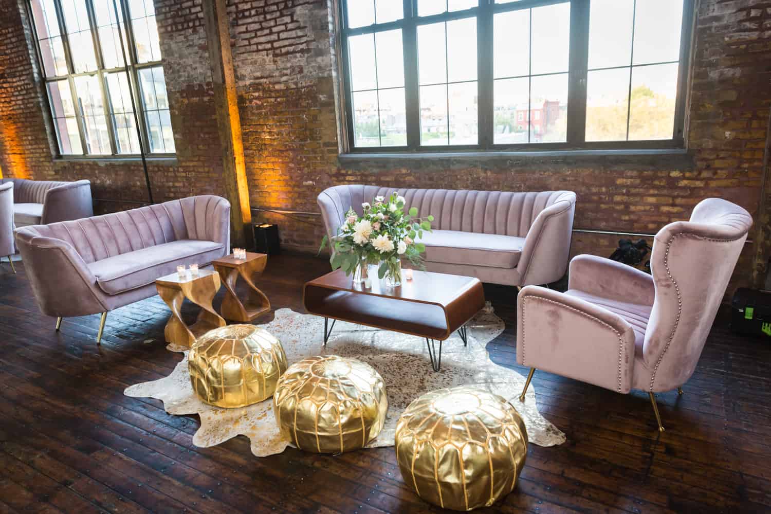 Pink velvet couches and gold poofs with coffee table at Greenpoint Loft wedding reception