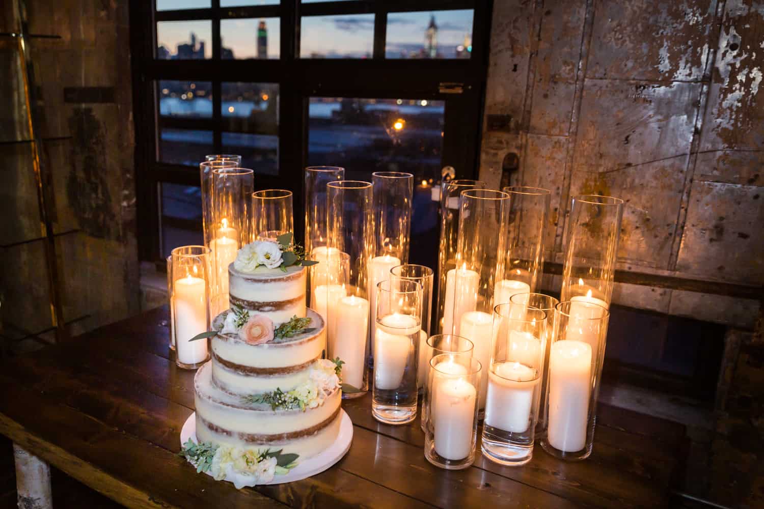 Wedding cake and rows of candles on table with view of NYC skyline through window