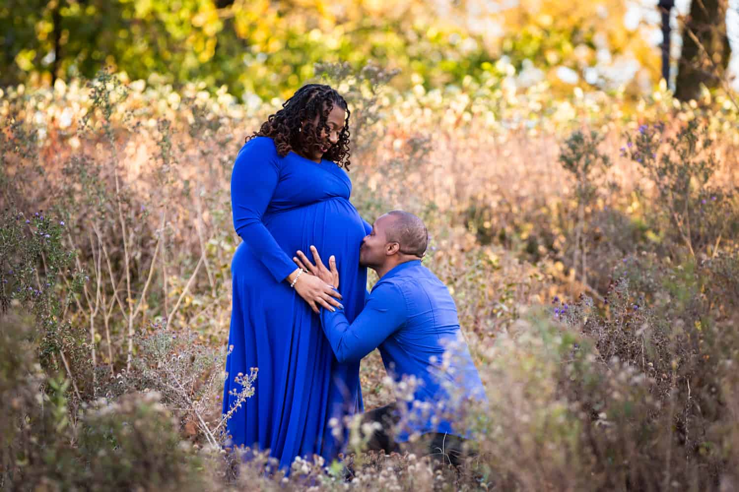 Man kissing wife's pregnant stomach in Forest Park during maternity photo shoot