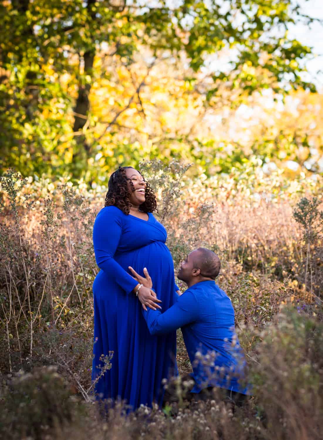 Man kneeling to kiss wife's pregnant stomach in Forest Park