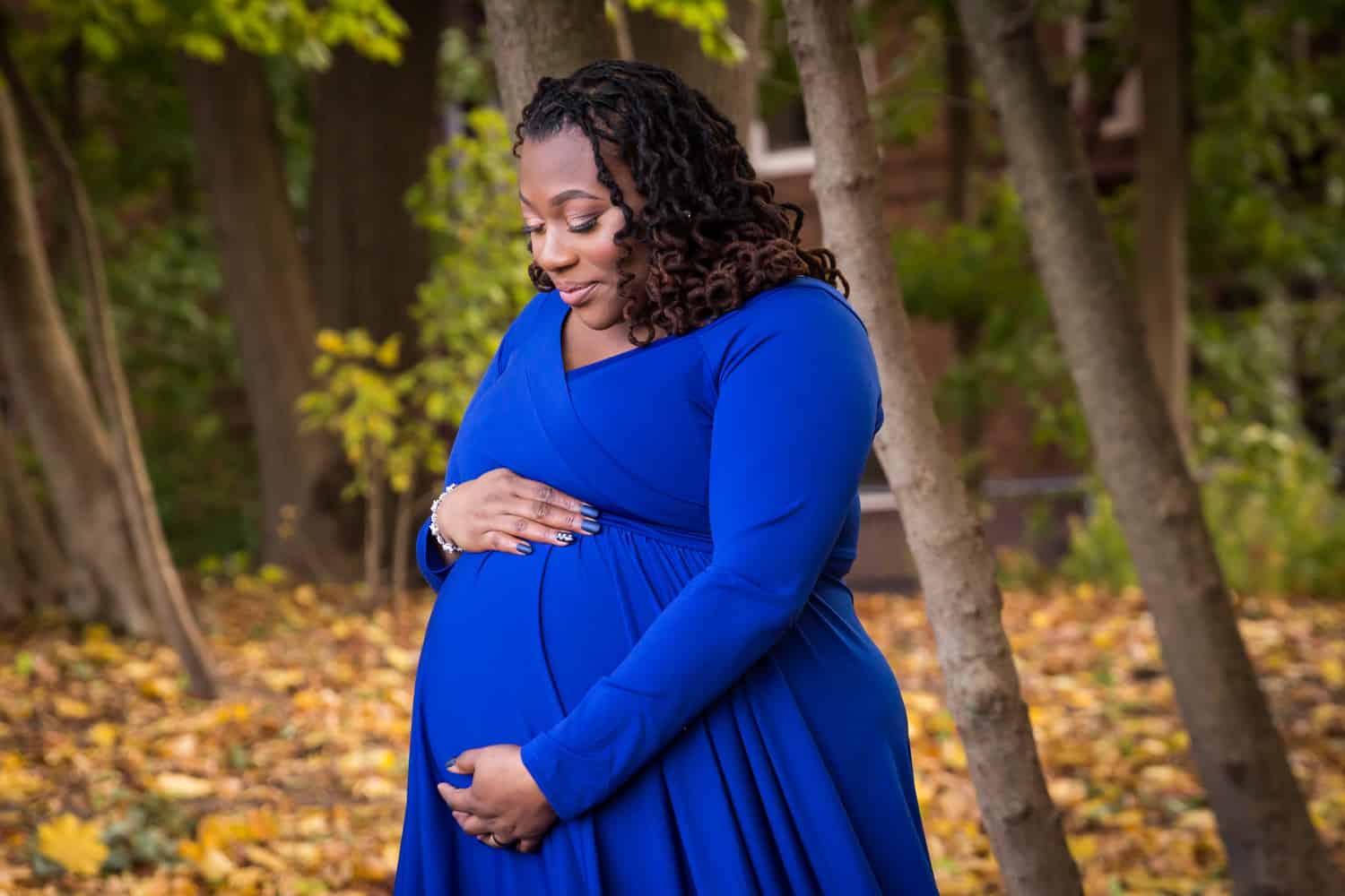 African American pregnant woman touching stomach and wearing blue dress in Forest Park