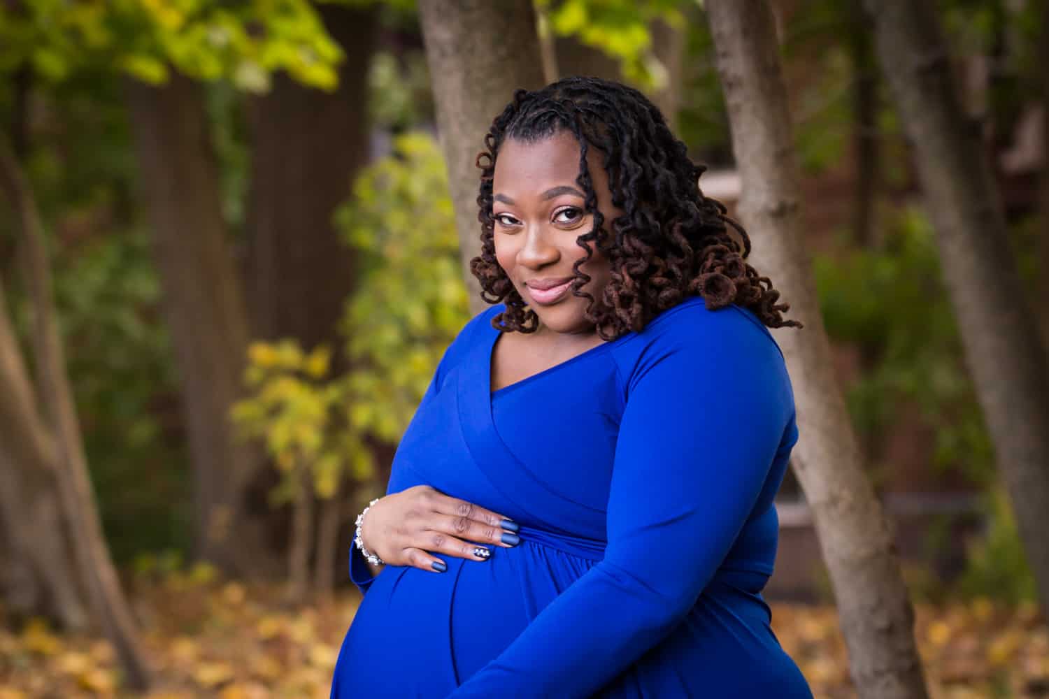 African American pregnant woman touching stomach and wearing blue dress in Forest Park