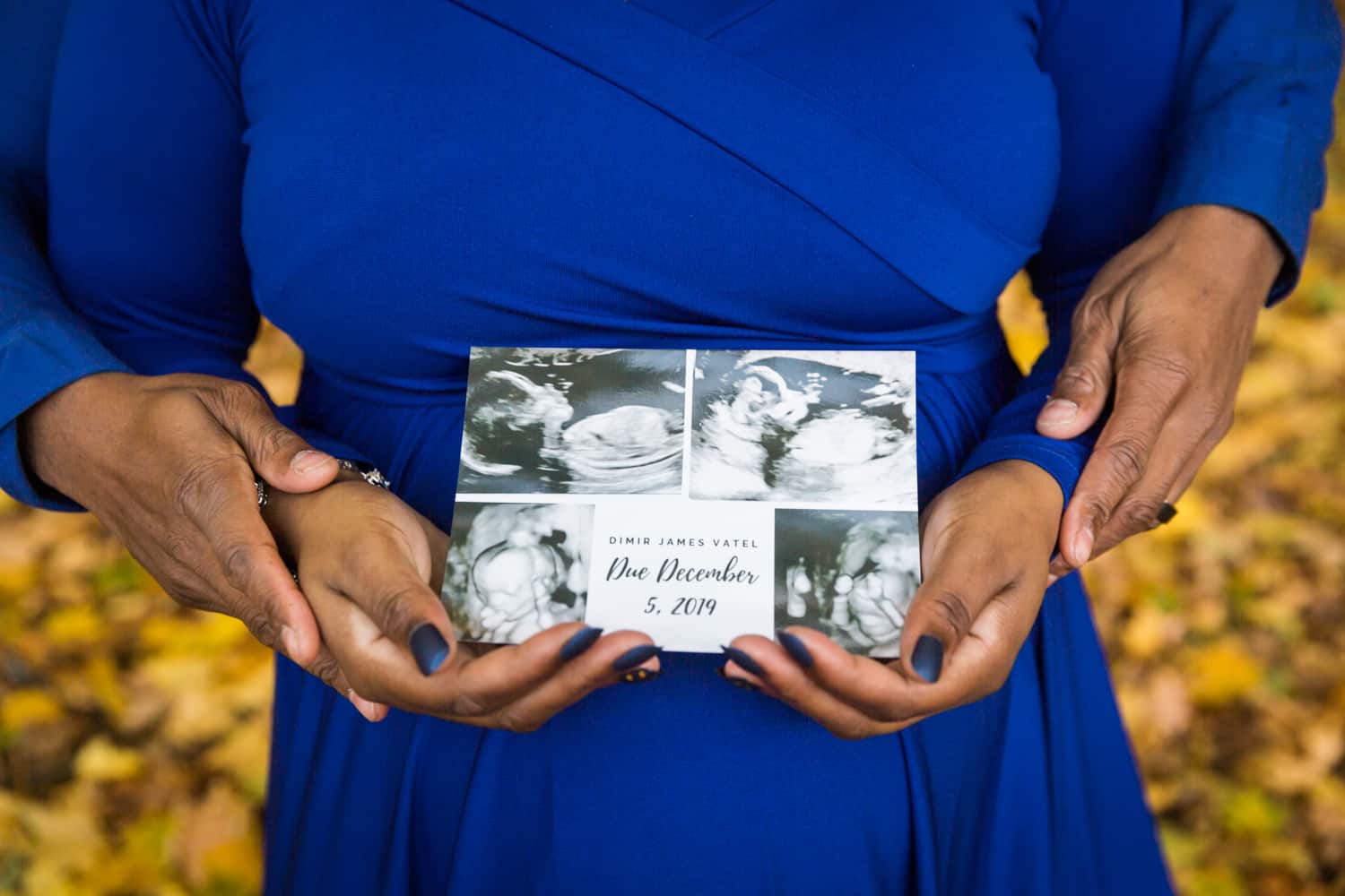 Close up of couple's hands on woman's pregnant stomach and holding birth announcement postcard