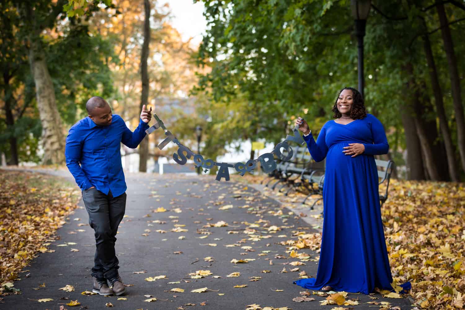 African American couple holding 'It's a Boy' sign in Forest Park pathway