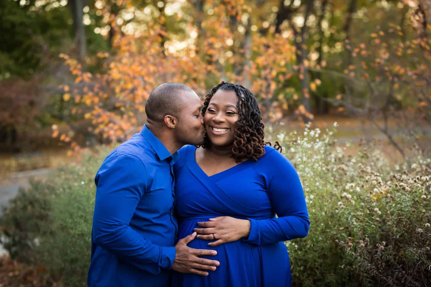 Man kissing woman's cheek during maternity photo shoot in Forest Park
