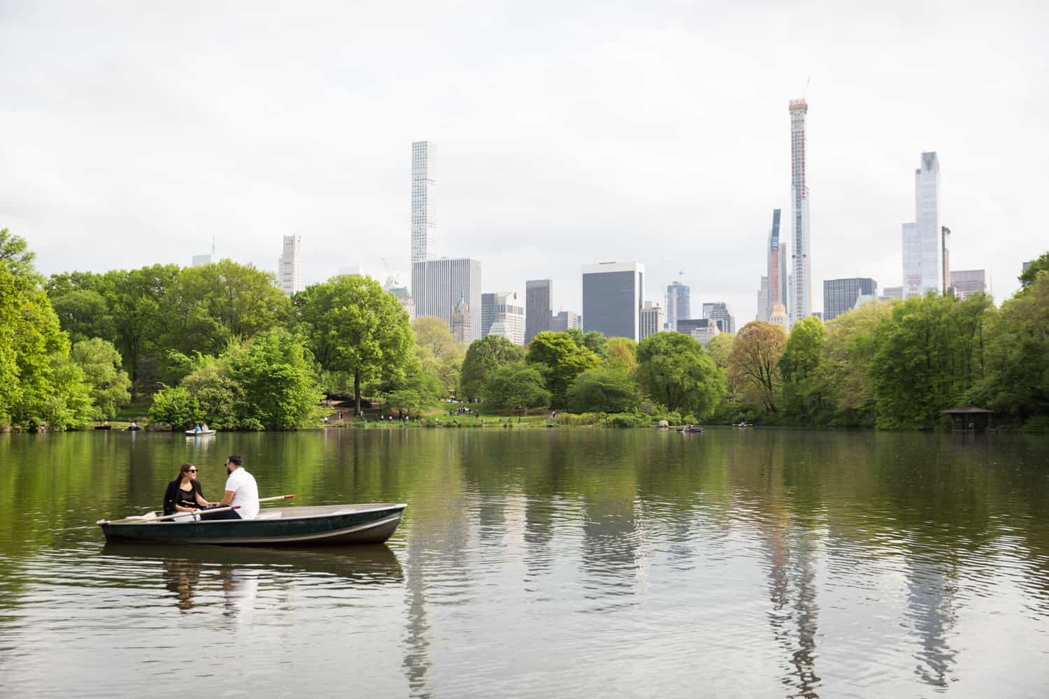 Couple in boat with NYC skyline in background at a surprise proposal on Central Park Lake