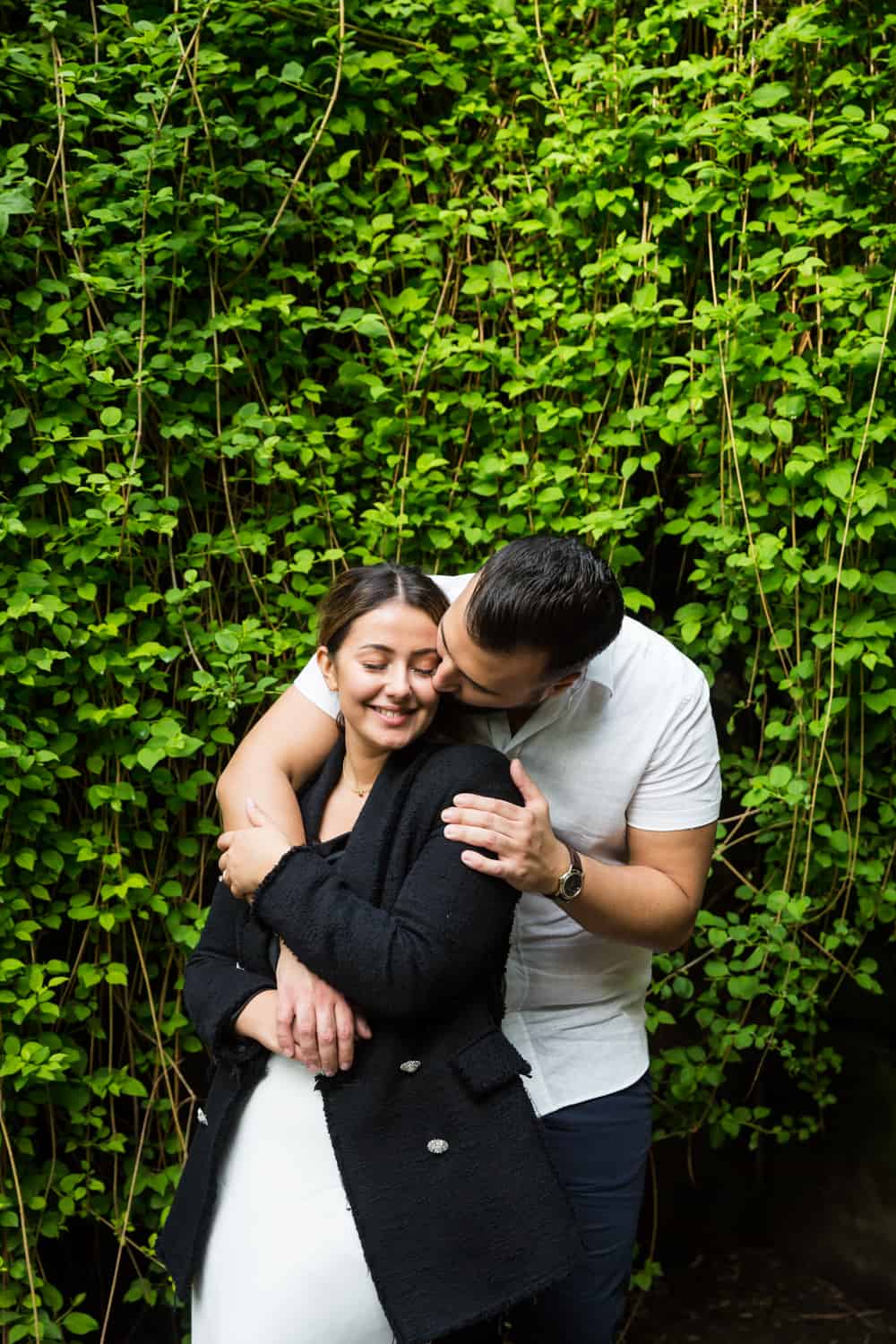Man kissing woman's cheek in front of ivy-covered wall