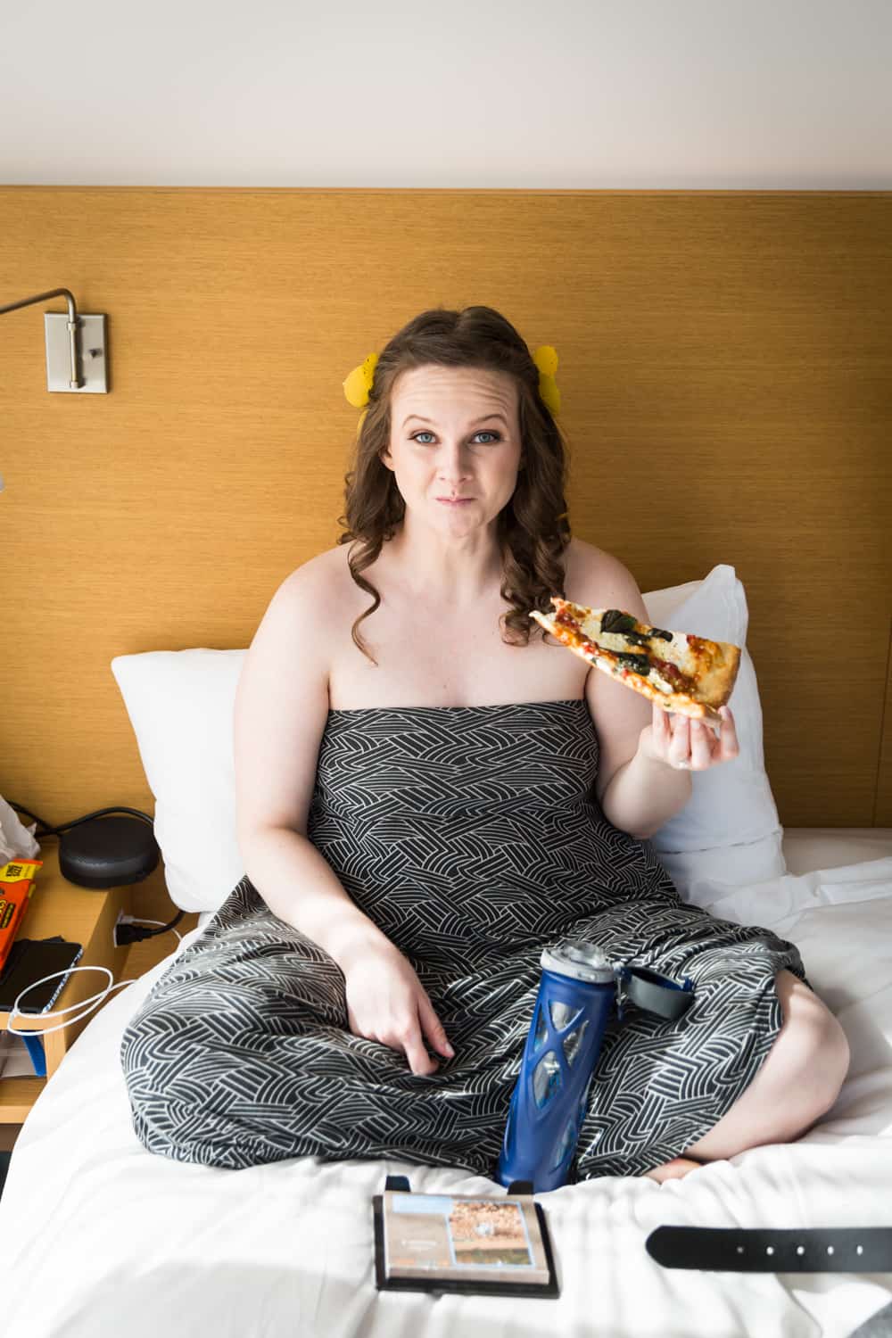 Bride sitting on bed eating slice of pizza
