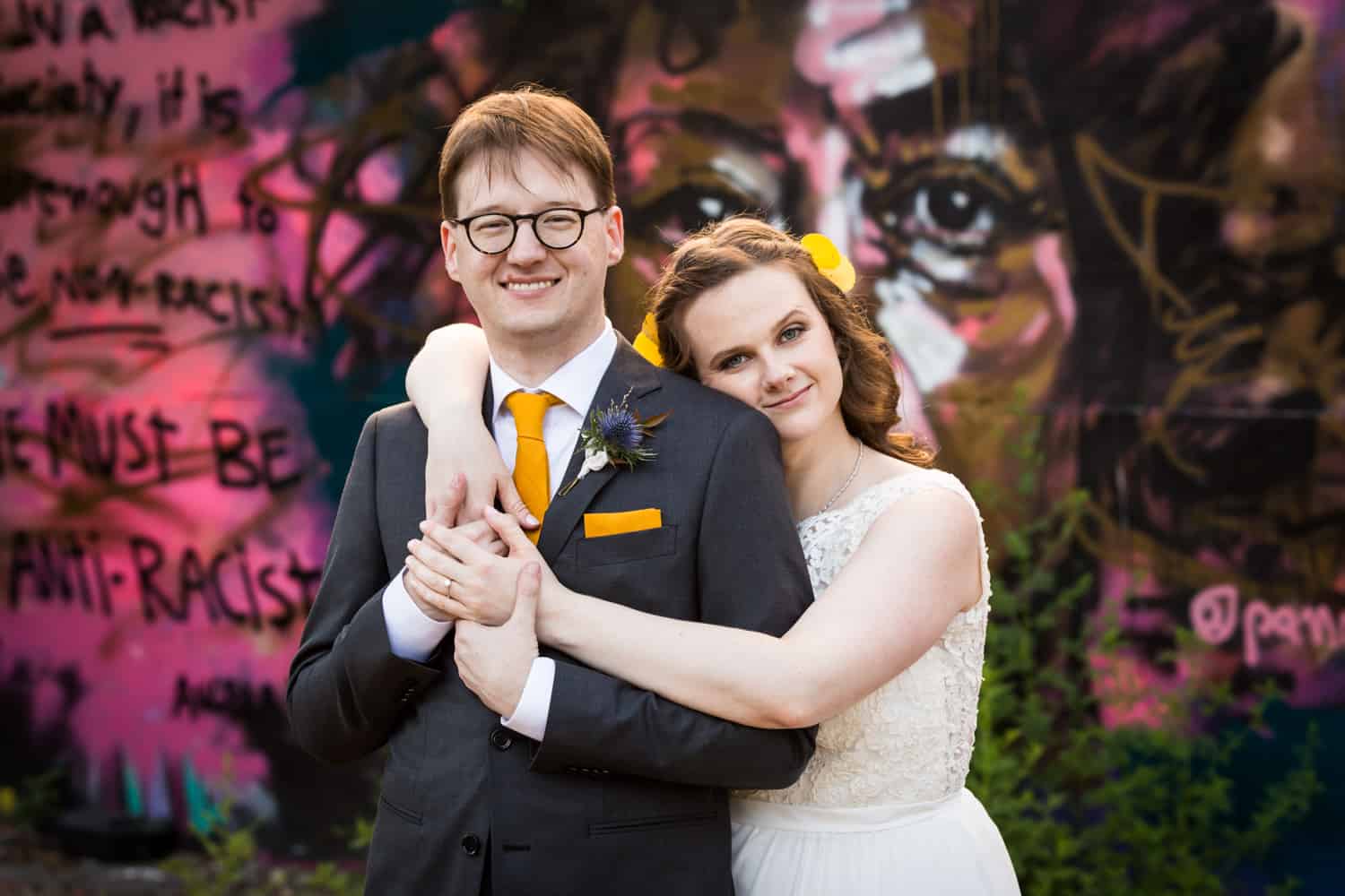 Bride hugging groom in front of graffiti for an article on Covid-19 wedding planning