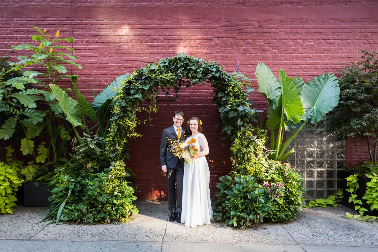 Bride and groom under arch of plants on NYC sidewalk