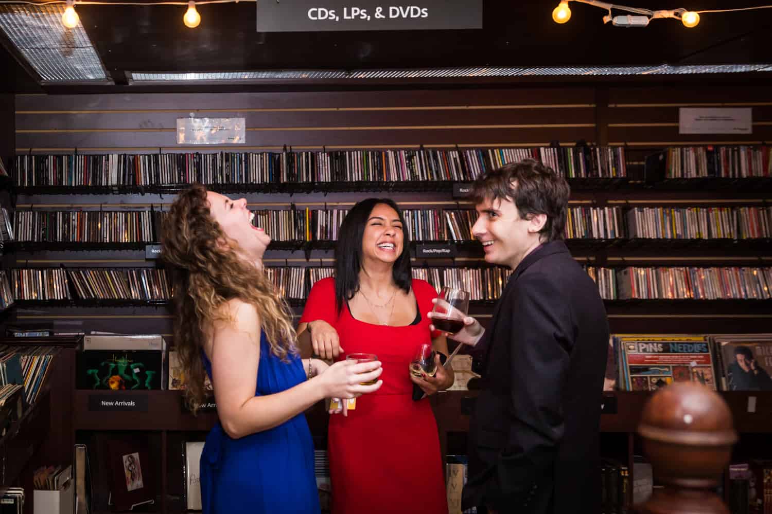 Three guests laughing in front of rows of CDs at a Housing Works Bookstore Cafe wedding