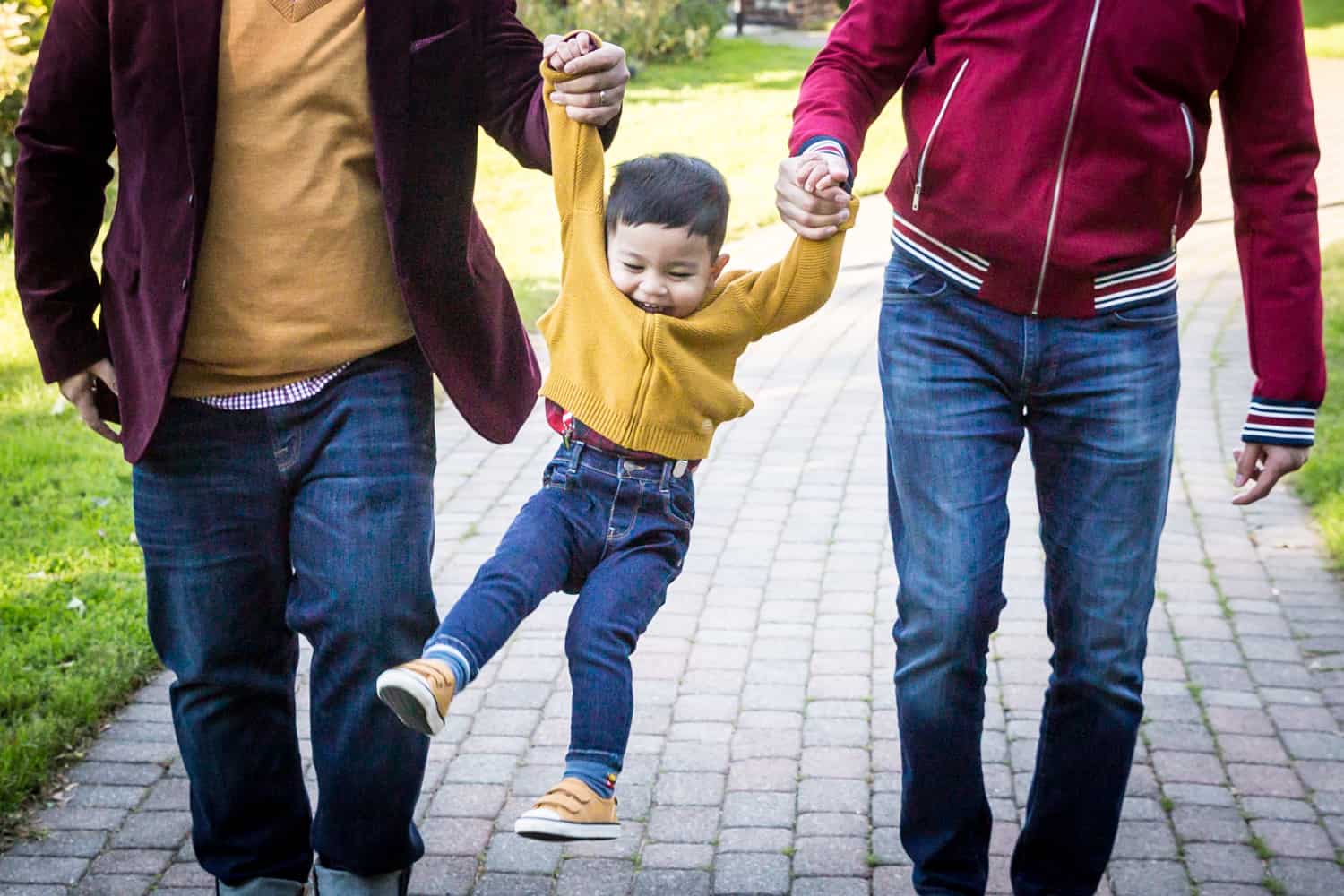 Close up of little boy being swung by arms by two fathers during a Great Neck family portrait session