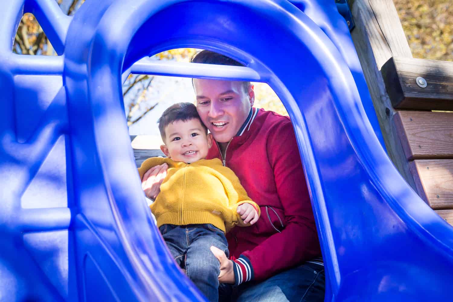 Father playing with little boy on blue slide