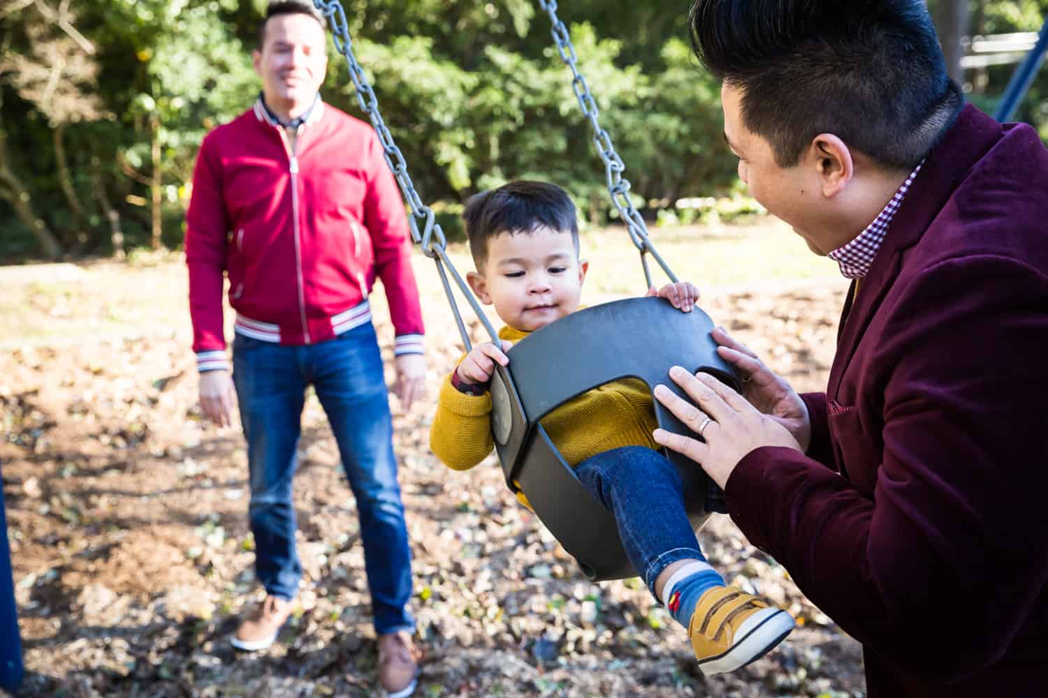Two gay fathers playing with little boy on swing in playground