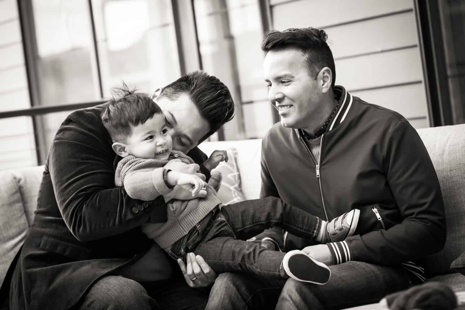 Black and white photo of two gay fathers playing with little boy