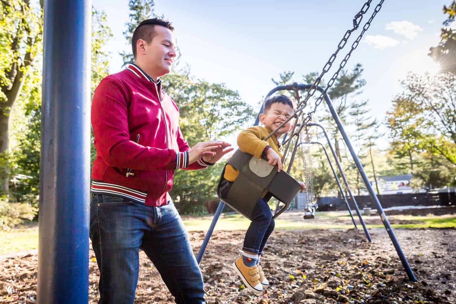 Father playing with little boy on swing in playground